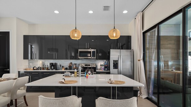 Une cuisine moderne avec des meubles de couleur sombre, un grand îlot central et des luminaires suspendus.