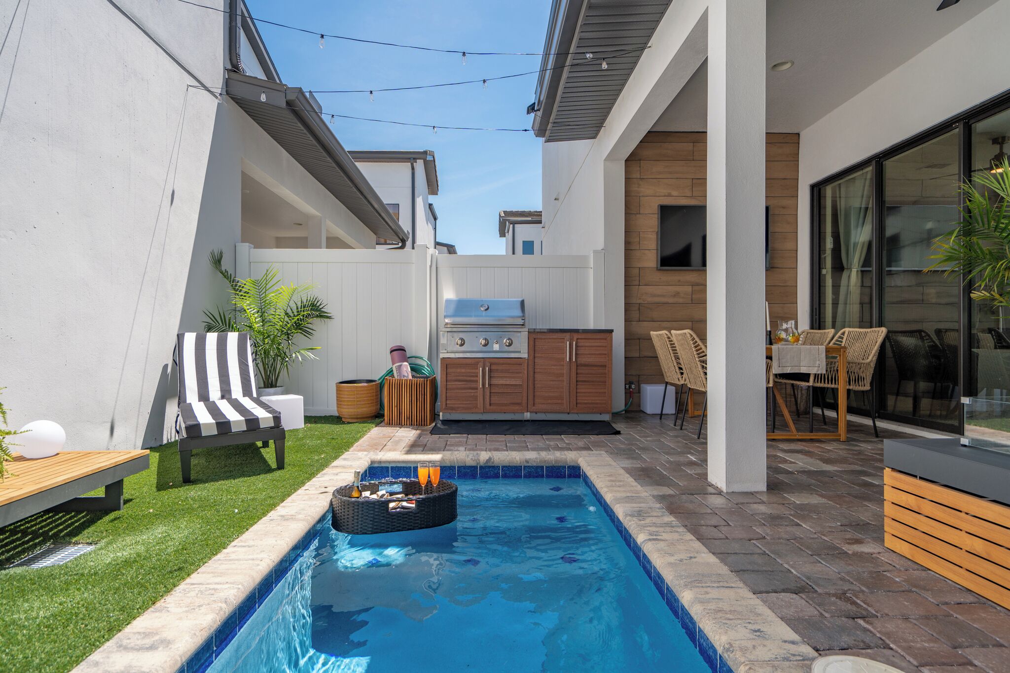 A modern backyard with a swimming pool, outdoor seating, and a kitchen area.