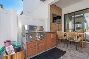 An outdoor kitchen with a grill, wooden cabinets, wicker chairs, and a dining table. - Tulum-Vibe Villa, 15 min to Disney, Pools, Master Suite, Billiards, Fireplace (Davenport)