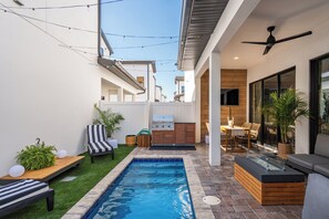 Un espacio exterior moderno con piscina, mobiliario y una barbacoa.
