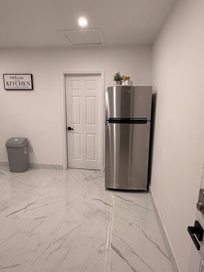 A kitchen with a stainless steel refrigerator, a trash bin, a white door, and a welcome sign on the wall. - Velvet Desire Only For adults/ 15 min Strip (Las Vegas)