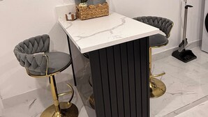 A modern dining area with a marble countertop, two upholstered chairs with gold legs, a small side table with a vase, and a floor lamp. - Velvet Desire Only For adults/ 15 min Strip (Las Vegas)