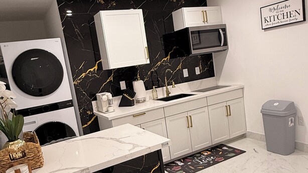 A modern kitchen with a marble countertop, a built-in washing machine, a microwave, and a grey trash bin. - Velvet Desire Only For adults/ 15 min Strip (Las Vegas)