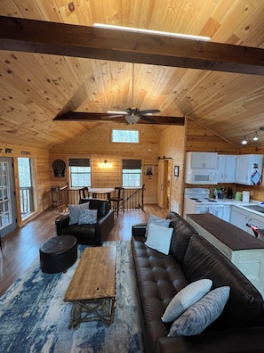 A cabin interior with a living room, dining area, kitchen, and a ceiling fan. - 
Misty Spruce, tucked away, wooded oasis. (Gatlinburg)