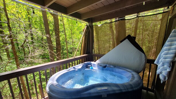 A hot tub on a wooden deck with a view of a forest. - 
Misty Spruce, tucked away, wooded for 2 guests. Honeymoon/Anniversary/Birthdays (Gatlinburg)
