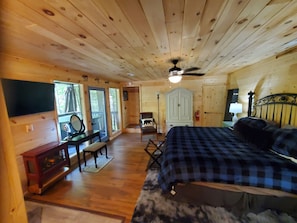 A wooden cabin interior with a bed, a desk, a chair, a wardrobe, and a television. - 
Misty Spruce, tucked away, wooded oasis. (Gatlinburg)