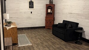 A room with a wooden floor, a black sofa, a small table, a cabinet, and a wall-mounted light fixture.