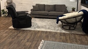 A living room with a sofa, a recliner, a floor lamp, a rug, and a wall-mounted air conditioner.