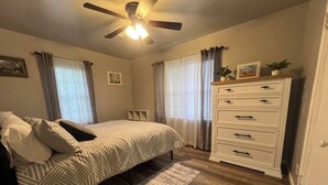 A bedroom with a bed, a dresser, a ceiling fan, and curtains.