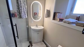 Un bagno con box doccia in vetro, lavandino, WC e mobile bagno con specchio.