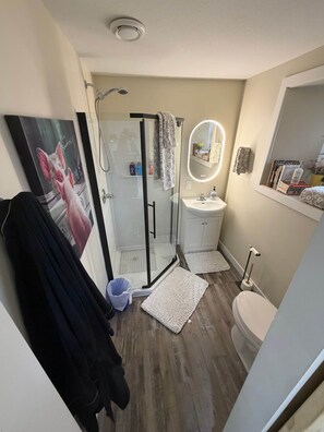 Un baño moderno con cabina de ducha de vidrio, lavamanos blanco, inodoro y espejo con luz.