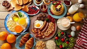 Een ontbijt met toast, pannenkoeken, eieren, worstjes en diverse soorten fruit en groenten.