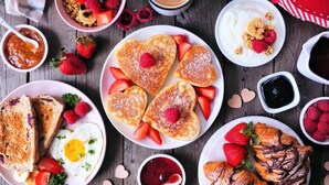 Diverse ontbijtproducten, zoals pannenkoeken, wafels, toast en gebak, op een houten tafel.
