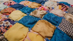 Een bed met een kleurrijke quilt en een effen kussen.
