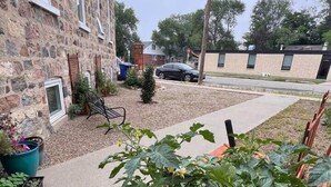 A residential area with a stone building, a garden with plants, and a street with cars and houses in the background. - Charming Bed & Breakfast! 2 (Estevan)