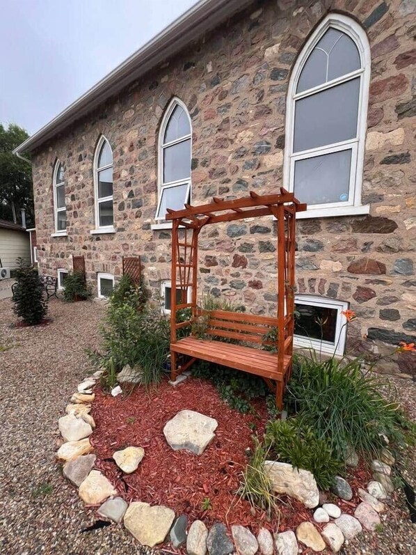A stone building with arched windows and a wooden bench in the garden.
