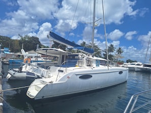 A marina with a white sailboat docked, surrounded by other boats, with a clear sky and palm trees in the background.