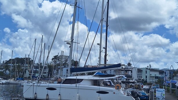 A marina with multiple sailboats docked, a clear sky, and buildings in the background. - Shared catamaran anchored in anse mitan bay at trois ilets (Les Trois-Îlets)
