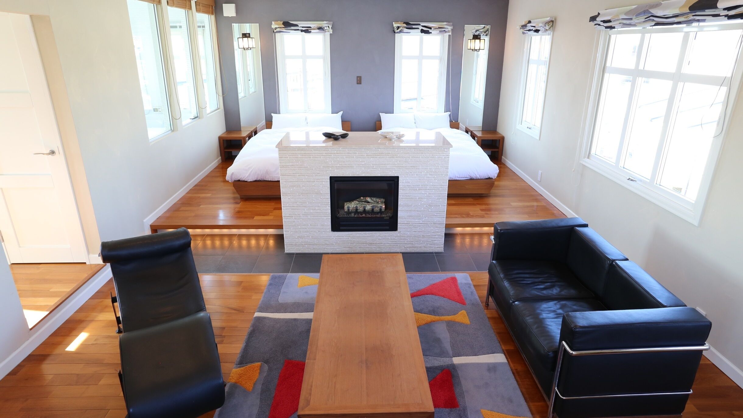 A modern hotel room with a large bed, a fireplace, a sofa, and a coffee table.