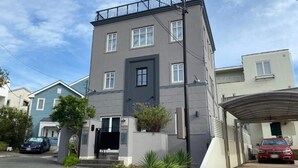 A multi-story residential building with a grey facade, a black door, and a garage with a car parked inside. - Tabinoteitaku Kamakura Yuigahama (Kamakura)