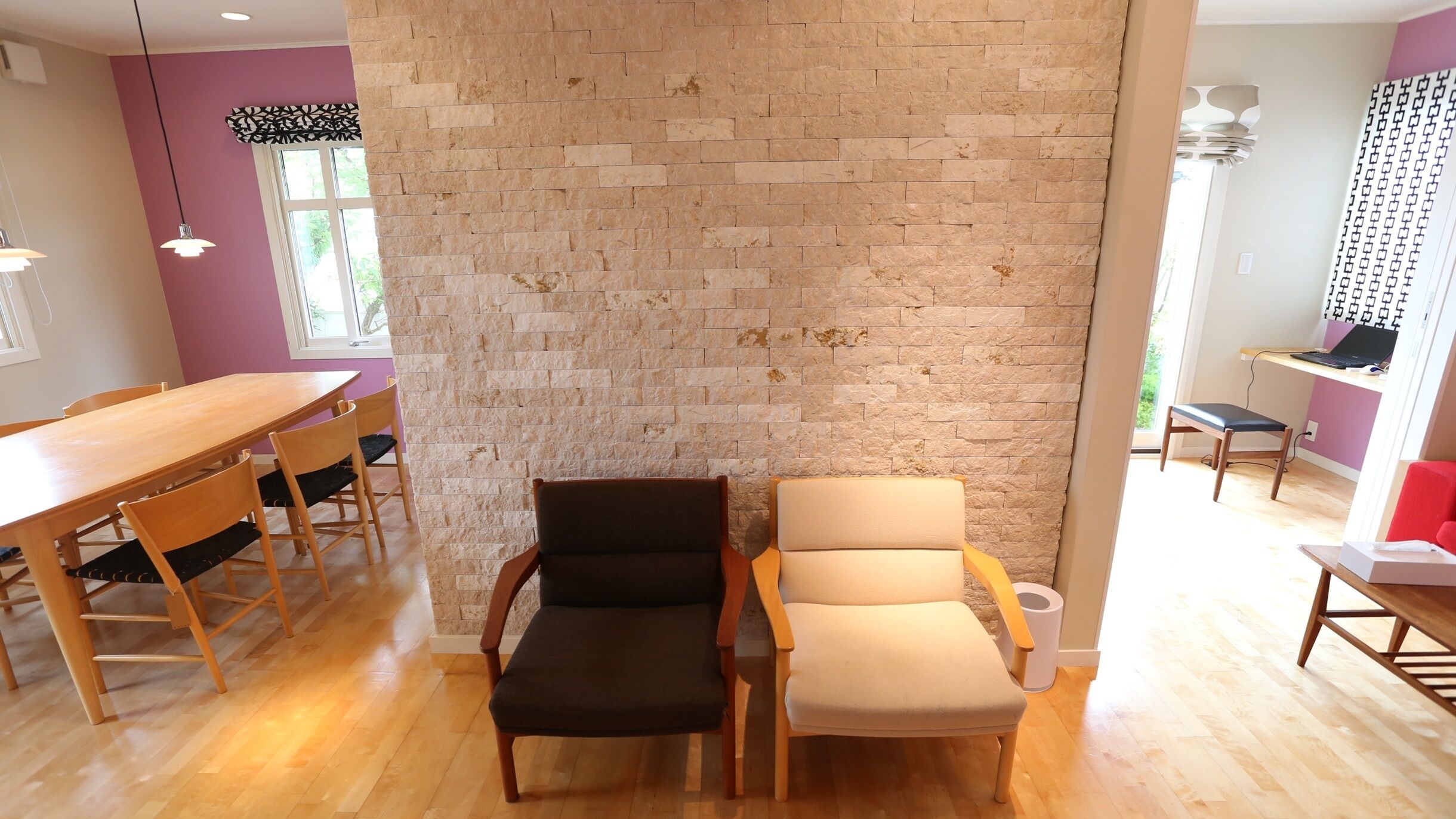 A dining area with a wooden table and chairs, a stone wall, and a window with natural light.