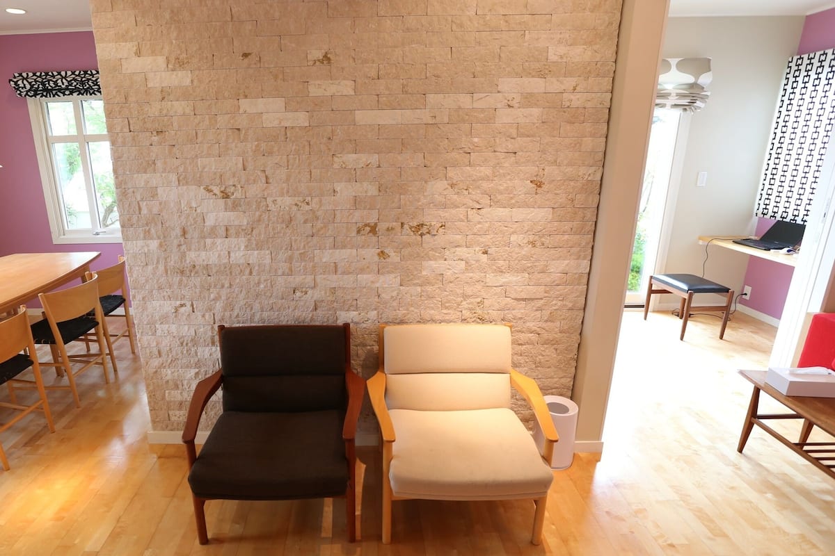 Un espace repas comprenant une table et des chaises en bois, un mur en pierre et une fenêtre laissant entrer la lumière naturelle.