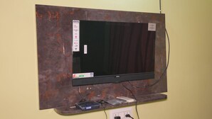 A flat-screen TV mounted on a wall with a soundbar, a power strip, and a cable management box. - Hotel Elite premium (Puri)