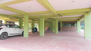 A covered parking area with a white car and a blue scooter, green pillars, and a stone wall. - Hotel Elite premium (Puri)