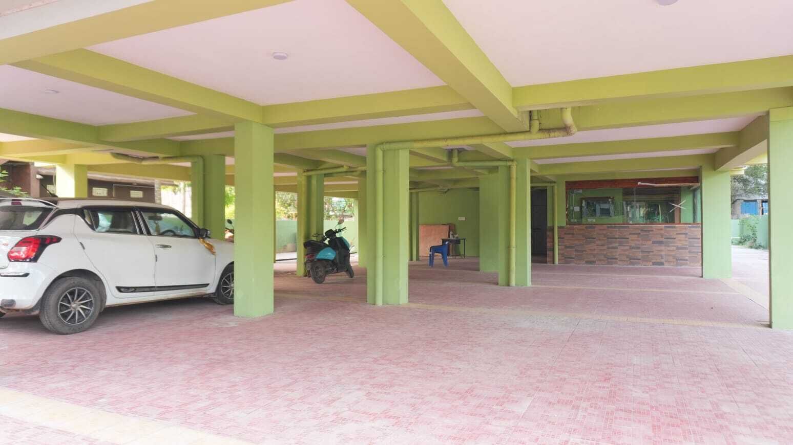 A covered parking area with a white car and a scooter, green pillars, and a stone wall.