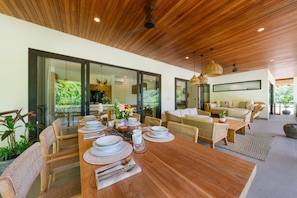 A modern dining area with a wooden table set for a meal, wicker chairs, and a sofa in the background.