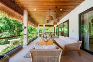 A modern outdoor living space with a wooden ceiling, wicker furniture, and a view of lush greenery.