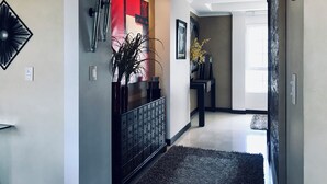 Un couloir avec un portail en métal noir, une décoration murale rouge et blanche, un vase noir contenant une plante et un tapis noir.