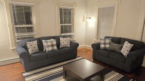 Ein Wohnzimmer mit zwei dunkelgrauen Sofas, einem dunkelholznen Couchtisch und einem Streifenmuster-Teppich.