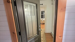 Eine holzrahmenverkleidete Tür führt zu einem Zimmer mit Teppichboden und einem sichtbaren Bett.