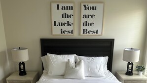 Un lit bien fait, avec du linge de lit blanc, deux tables de chevet avec des lampes et deux citations inspirantes encadrées accrochées au mur.