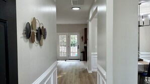 Un couloir avec un tapis à motifs, des lambris blancs, une porte dotée d’une poignée noire et un luminaire au plafond.