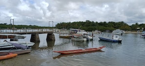 A marina with various boats docked, a bridge, and a beach with palm trees in the background. - PEDRO'S LITTLE HOUSE - 100 meters from the tractor stop (Cairu)