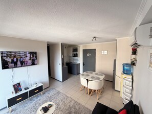 A modern living room with a flat-screen TV, a small table with a white rug, a sofa, and a water dispenser.