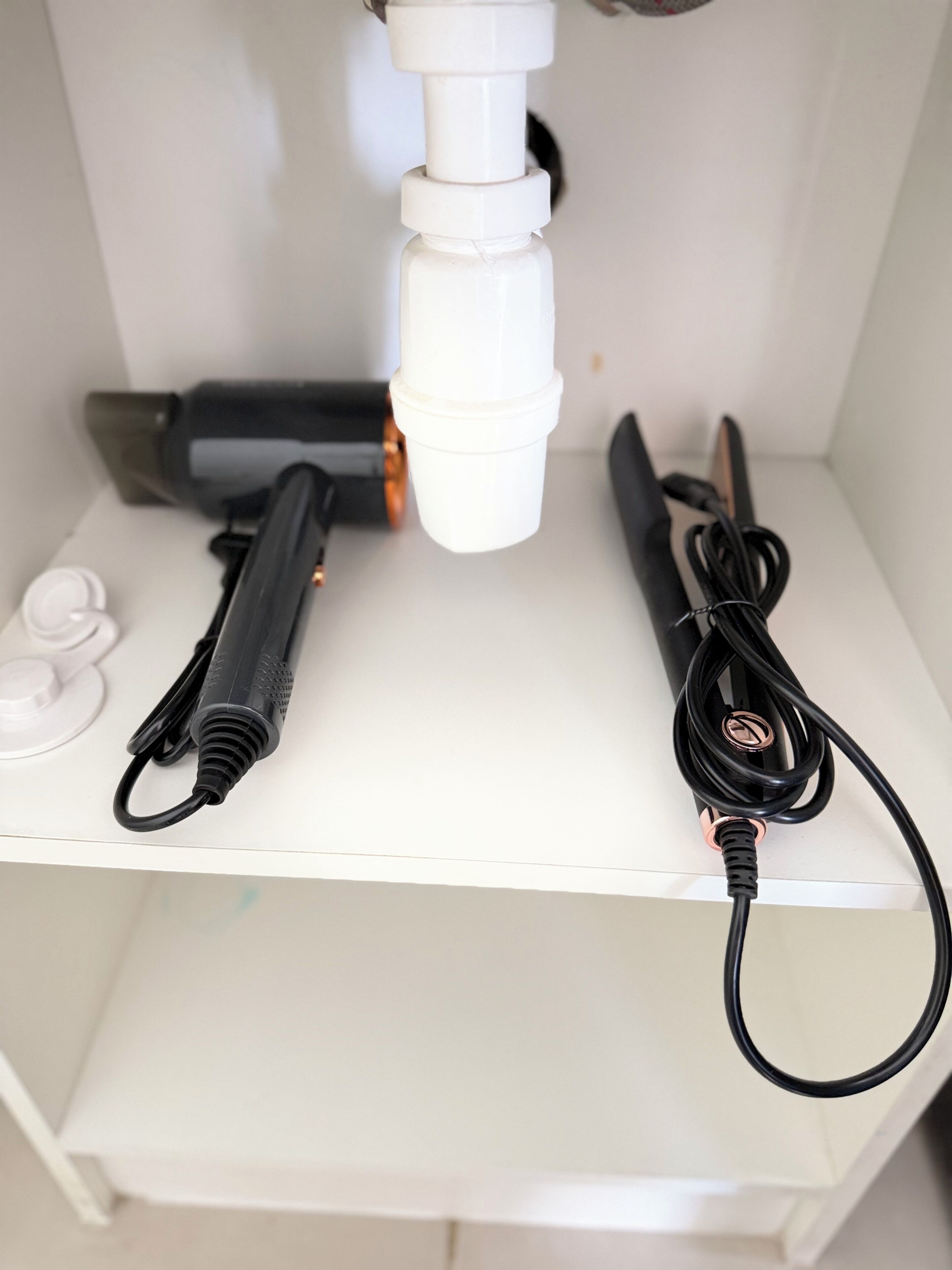 Uno scaffale bianco con un oggetto cilindrico bianco, un oggetto cilindrico nero e un cavo nero con un connettore metallico.