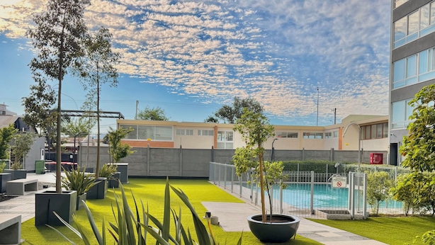 Eine Dachgartenanlage mit Kunstgrasanlage, Topfpflanzen, einem Pool und modernen Gebäuden im Hintergrund.