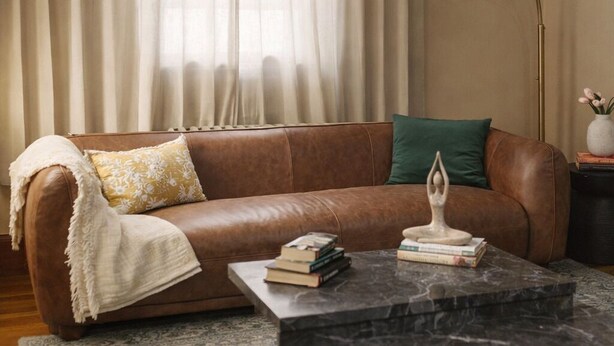 A brown leather sofa with a throw blanket, a green pillow, and a marble coffee table with books. - Elegant 4BDR Boston Stay Free Garage + EV Charger (Boston)