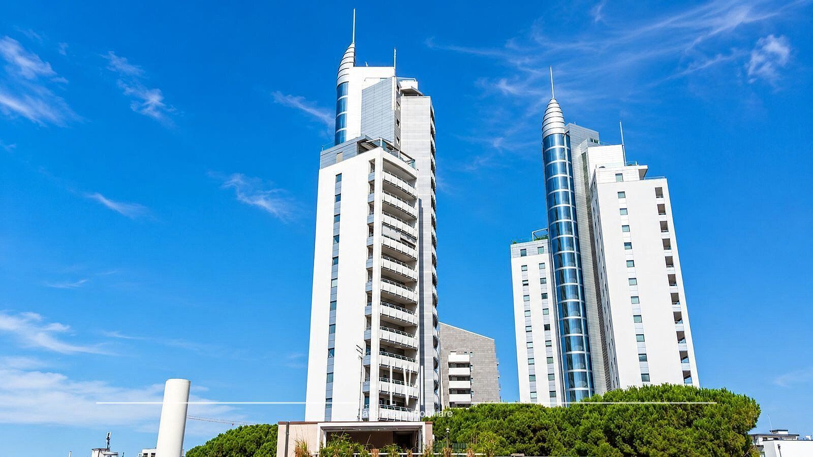 Dois edifícios modernos altos com varandas, sob um céu azul límpido.