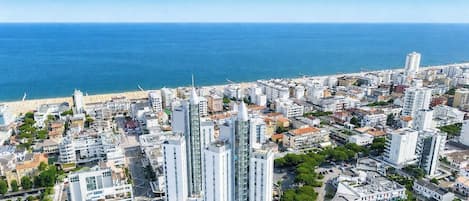 A coastal cityscape with modern buildings, a beach, and a clear view of the sea.