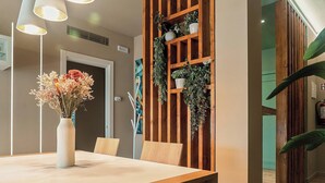 Uma sala de jantar com uma mesa, cadeiras, um vaso com flores e um painel de madeira com plantas.