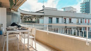 Uma varanda com uma mesa e cadeiras de jantar, vista de um edifício com varandas e céu claro.