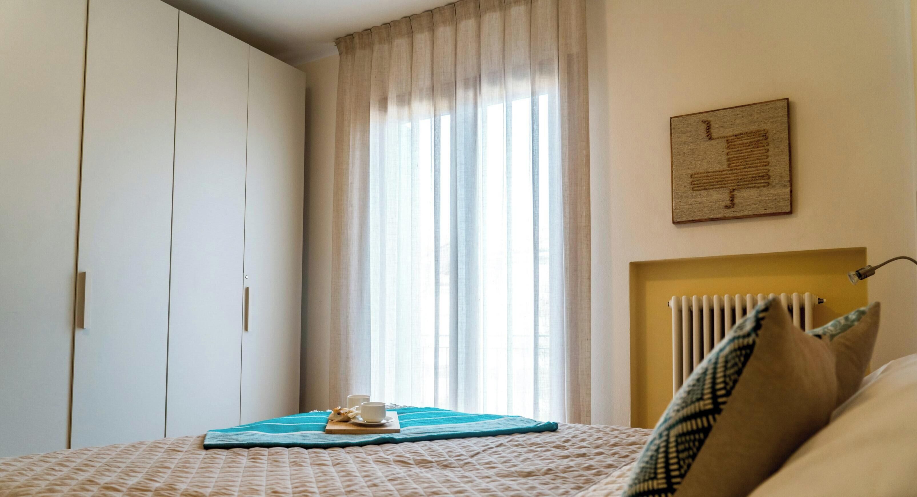 Un dormitorio con una cama, un radiador, una ventana con cortinas y una obra de arte colgada en la pared.