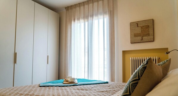 Une chambre à coucher avec un lit, un radiateur, une fenêtre avec des rideaux et une œuvre d’art accrochée au mur.