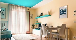 Un coin repas avec une table dressée pour deux personnes, une étagère bleue au-dessus et une vue sur la pièce adjacente.
