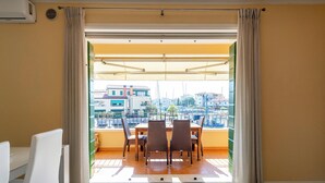 Uma varanda com mesa e cadeiras, vista para um horizonte urbano com edifícios e um porto.