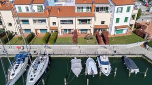 Um edifício de vários andares com varandas, uma marina com barcos e um céu limpo.